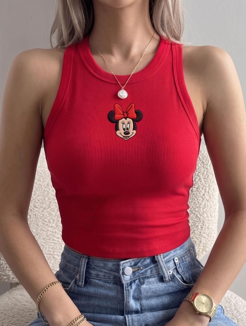 K&ouml;nnte beinhalten: Ein rotes geripptes Tanktop mit einem Minnie Mouse-Patch mit roter Schleife. Das Oberteil ist &auml;rmellos und hat einen runden Ausschnitt. Die Person tr&auml;gt eine Jeans und eine goldene Halskette.