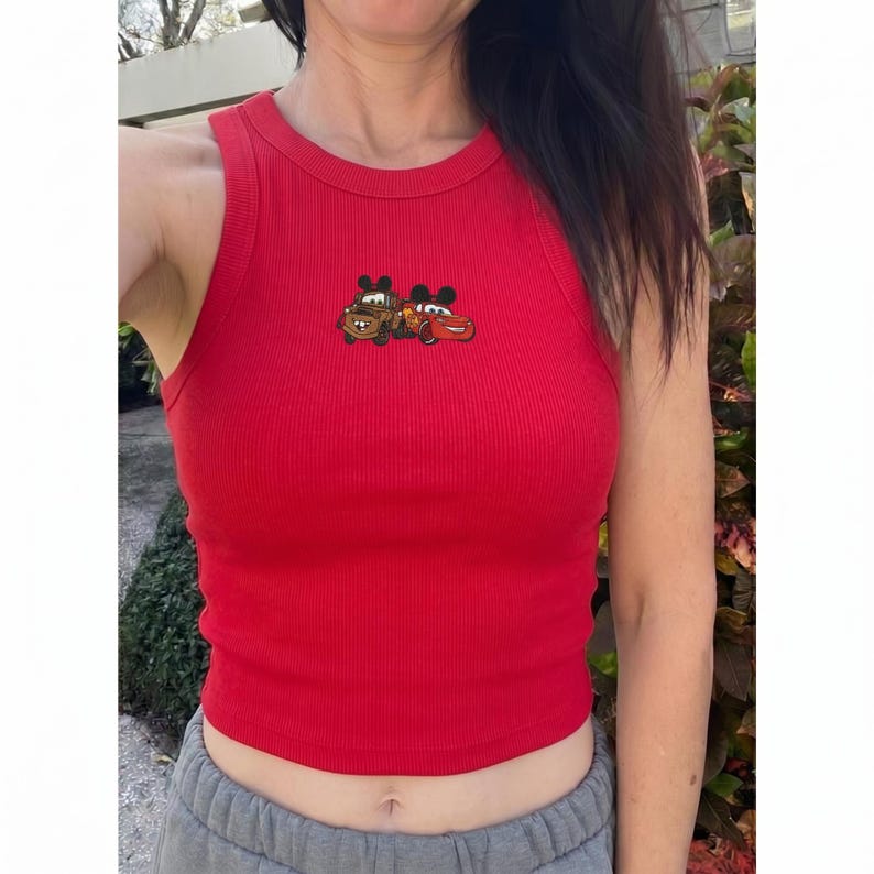 May include: A red ribbed tank top featuring a graphic of two cartoon cars. The sleeveless top has a crew neck and is made of a soft, stretchy material. The graphic is located on the upper chest area.