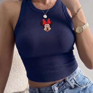 K&ouml;nnte beinhalten: Marineblaues geripptes Tanktop mit Minnie Mouse Applikation und roter Schleife. Dazu blaue Jeans. Eine goldene Halskette und Uhr erg&auml;nzen den Look und bieten eine l&auml;ssige, aber stilvolle &Auml;sthetik.
