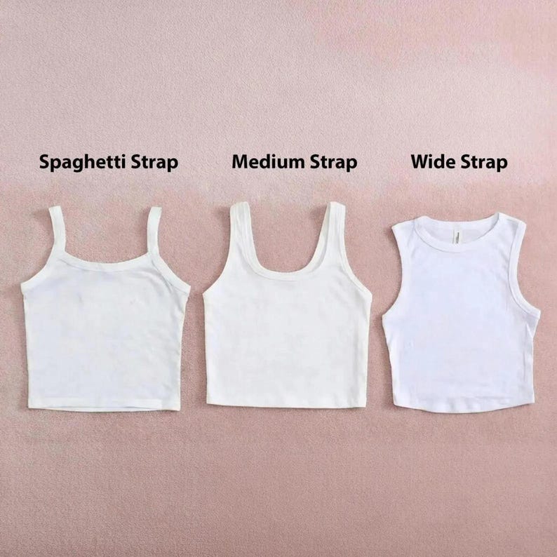 May include: Three white crop tops with different strap styles: spaghetti strap, medium strap, and wide strap. The tops are displayed on a pink background, showcasing the variations in design. The text labels each style.
