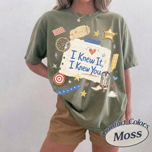 Puede incluir: Una camiseta de manga corta color verde oliva con un gr&aacute;fico central de papel de cuaderno rayado con el texto azul I Knew It, I Knew You. El dise&ntilde;o incluye una bota de vaquero, una estrella de sheriff, una rueda de carreta y varios iconos.
