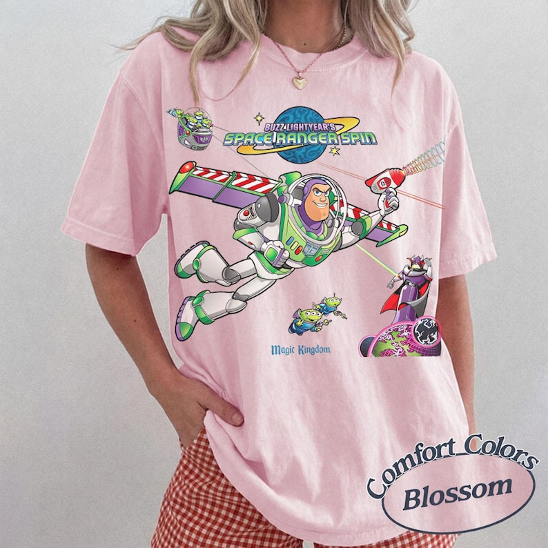 May include: Pink Comfort Colors t-shirt featuring a graphic of Buzz Lightyear from Toy Story. The design includes the text "Buzz Lightyear's Space Ranger Spin" and "Magic Kingdom". The shirt has short sleeves and a relaxed fit.