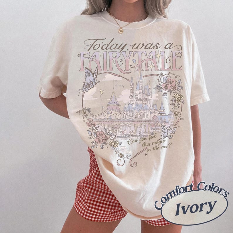 Może przedstawiać: T-shirt w kolorze kości słoniowej z nadrukiem graficznym zawierającym tekst "Today was a FAIRY TALE" oraz "Can you feel this magic in the air?". Wz&oacute;r przedstawia zamek, motyle i elementy kwiatowe w delikatnych pastelowych odcieniach.