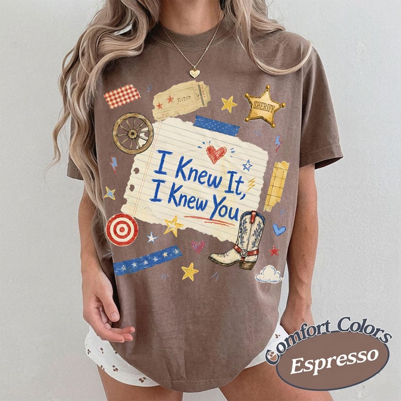 Puede incluir: Una camiseta marr&oacute;n de manga corta con un gr&aacute;fico central de papel de cuaderno rayado con el texto 'I Knew It, I Knew You' en azul. El dise&ntilde;o incluye una bota de vaquero, una estrella de sheriff, una rueda de carro, un ticket y estrellas.
