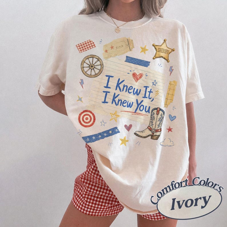 Puede incluir: Una camiseta de color marfil con un gr&aacute;fico central de un bloc de notas con l&iacute;neas y el texto I Knew It, I Knew You. El dise&ntilde;o incluye una bota de vaquero, una estrella de sheriff, una rueda de carreta, un boleto y varias estrellas, corazones y rayos.