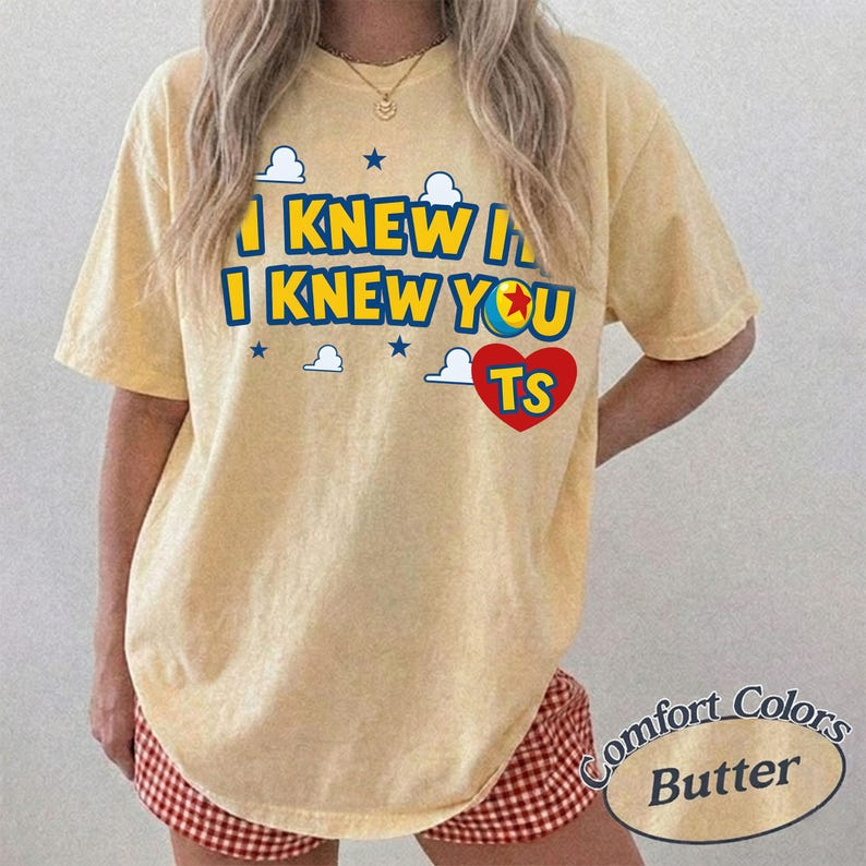K&ouml;nnte beinhalten: Ein blassgelbes Kurzarm-T-Shirt mit dem blauen Schriftzug I KNEW IT I KNEW YOU, einer bunten Ballgrafik mit rotem Stern, einem roten Herz mit den Buchstaben TS sowie kleinen wei&szlig;en Wolken- und blauen Sternsymbolen auf der Vorderseite.