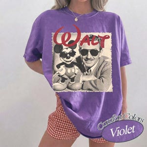 May include: Violet Comfort Colors t-shirt featuring a vintage graphic of Walt Disney and Mickey Mouse wearing sunglasses. The word "Walt" is in red script above the image. The shirt is paired with red and white checkered shorts.