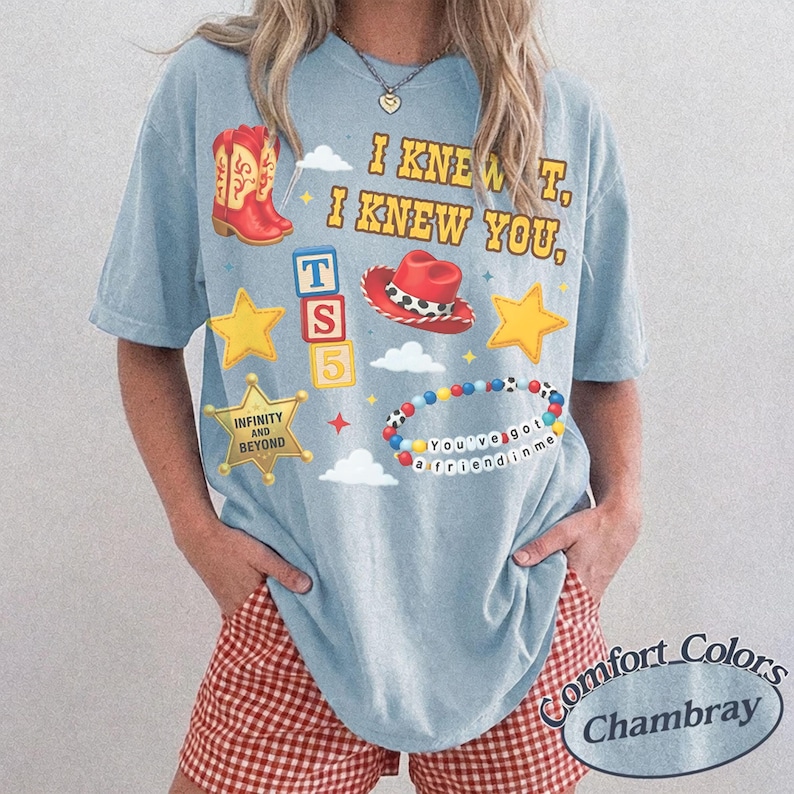 Pode incluir: Uma t-shirt de manga curta azul-clara com uma estampa gr&aacute;fica com o texto I KNEW IT, I KNEW YOU, uma bota de cowboy vermelha, um chap&eacute;u de cowboy vermelho, estrelas amarelas, uma estrela de xerife com INFINITY AND BEYOND, blocos e pulseira.