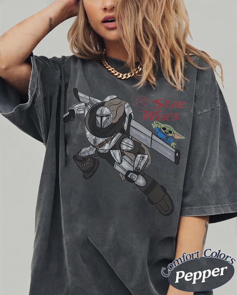 Pu&ograve; includere: T-shirt grigio scuro con una grafica di The Mandalorian e Grogu di Star Wars. Il design include il logo di Star Wars e il testo "Comfort Colors Pepper". La maglietta ha maniche corte e una vestibilit&agrave; ampia.