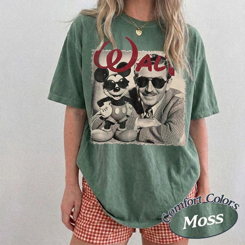 May include: A moss green t-shirt featuring a black and white image of Mickey Mouse and Walt Disney. The word "Walt" is printed in red script above the image. The shirt has a relaxed fit and is paired with red and white checkered shorts.