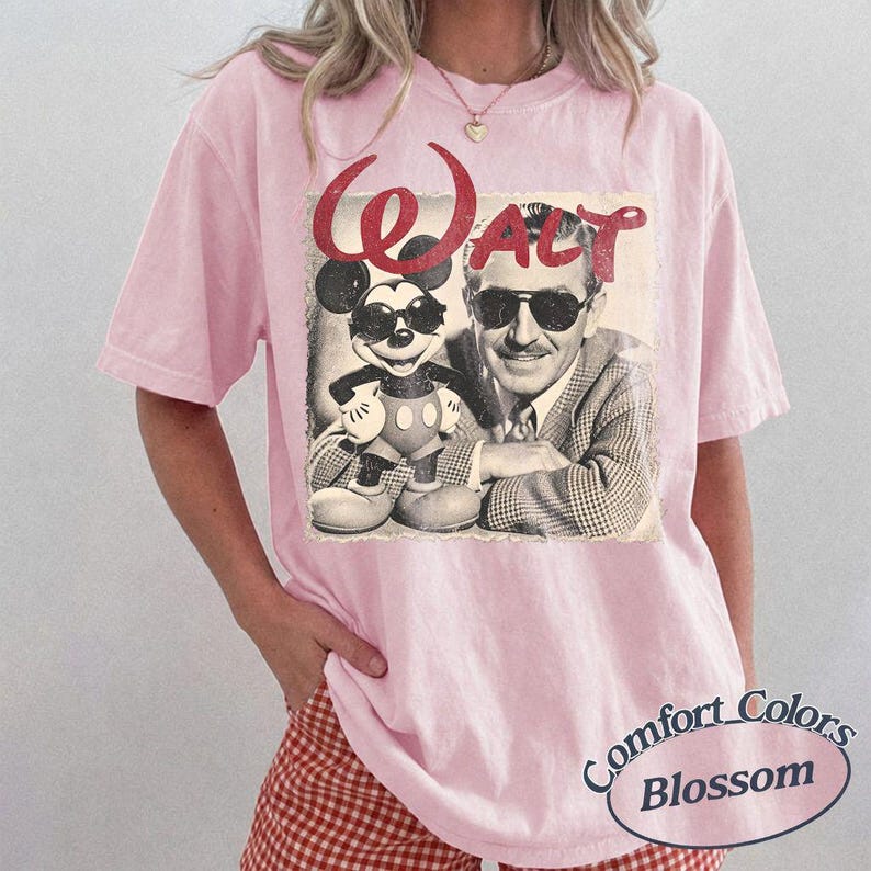 May include: Pink t-shirt featuring a vintage graphic of Mickey Mouse and Walt Disney with the word "Walt" in red. The shirt has a crew neck and short sleeves. The bottom right corner of the shirt has the words "Comfort Colors Blossom" in a circular design.