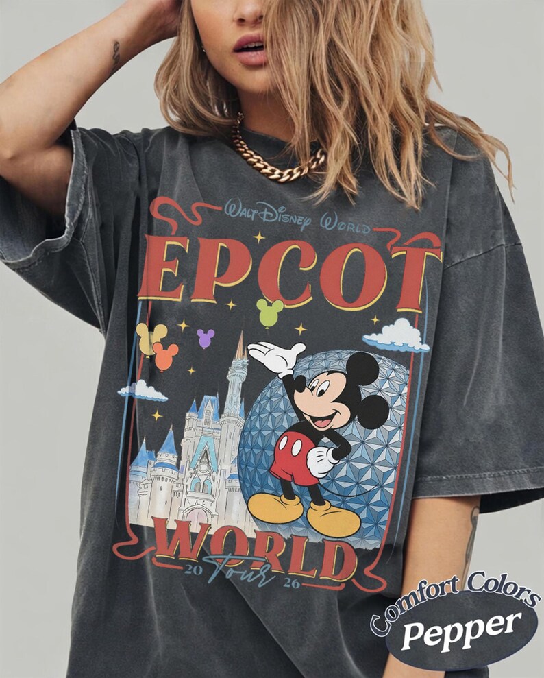 以下が含まれることがあります： Walt Disney World EPCOT World 20 Tour 26のテキストがプリントされたチャコールグレーの半袖Tシャツ。ミッキーマウス、エプコットのジオデシック・スフィア、城、そしてカラフルな風船のイラストが描かれています。
