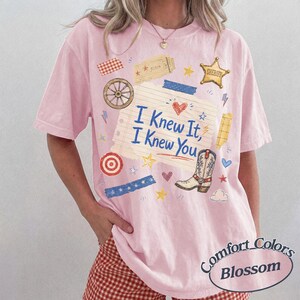 Puede incluir: Una camiseta de manga corta de color rosa claro con un gr&aacute;fico central de papel de cuaderno rayado con el texto I Knew It, I Knew You. El dise&ntilde;o incluye una bota de vaquero, una estrella de sheriff, una rueda de carro y estrellas.