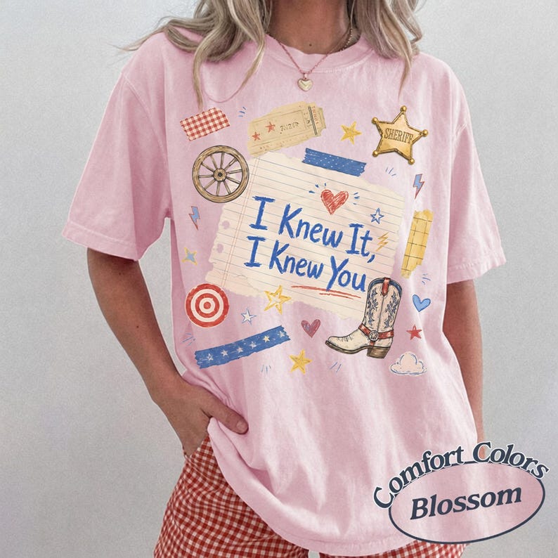 Puede incluir: Una camiseta de manga corta de color rosa claro con un gr&aacute;fico central de papel de cuaderno rayado con el texto I Knew It, I Knew You. El dise&ntilde;o incluye una bota de vaquero, una estrella de sheriff, una rueda de carro y estrellas.