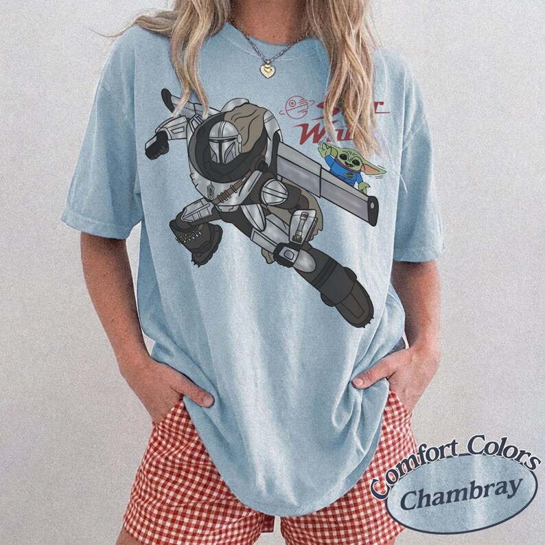 Pu&ograve; includere: T-shirt azzurra con una grafica di The Mandalorian e Grogu di Star Wars. Il design include il testo "Star Wars" in rosso. La maglietta &egrave; un Comfort Colors Chambray.