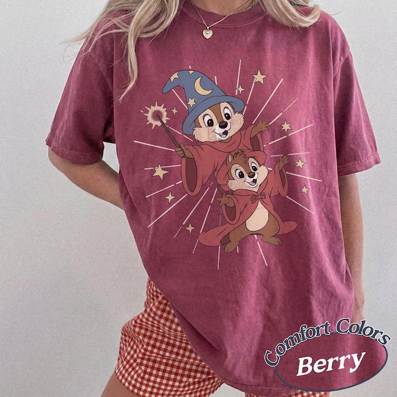 Op de afbeelding: Bessenkleurig T-shirt met een cartoon tovenaarsontwerp. De afbeelding toont twee eekhoorn-personages in tovenaarsgewaden en -hoeden, met een toverstaf en een sterrenburst-effect. Op het shirt staan de woorden "Comfort Colors" en "Berry".