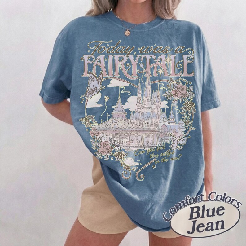 Może przedstawiać: Niebieski t-shirt z kr&oacute;tkim rękawem z nadrukiem graficznym przedstawiającym zamek, motyle i r&oacute;że. Tekst głosi Today was a FAIRY TALE oraz Can you feel this magic in the air? Koszulka ma okrągły dekolt i luźny, swobodny kr&oacute;j.