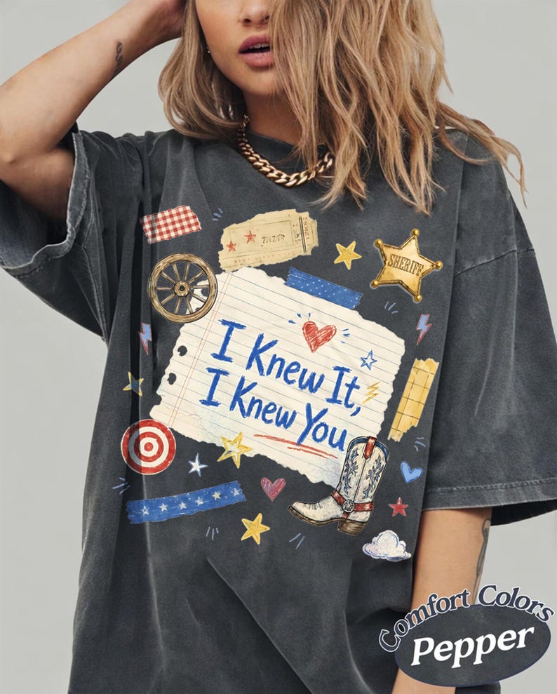 Puede incluir: Una camiseta gris carb&oacute;n con un gr&aacute;fico central de una p&aacute;gina de cuaderno rasgada con el texto "I Knew It, I Knew You" en azul. El dise&ntilde;o incluye una bota de vaquero, una estrella de sheriff, una rueda de carreta y peque&ntilde;os iconos.