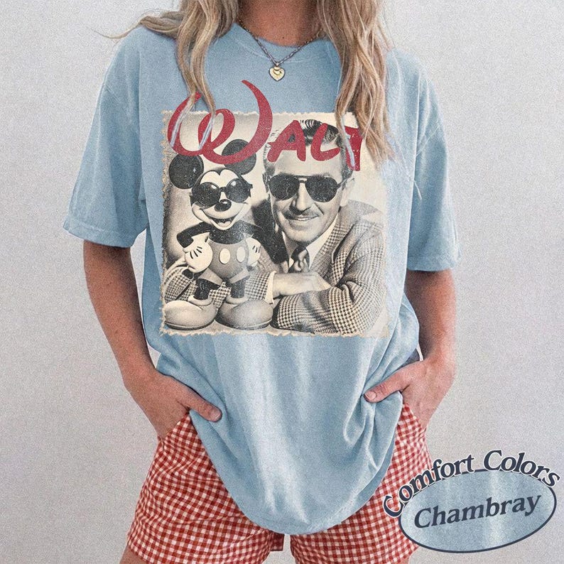May include: Light blue t-shirt featuring a vintage graphic of Mickey Mouse and Walt Disney. The graphic is in black and white with the word "WALT" in red. The shirt is a Comfort Colors Chambray.