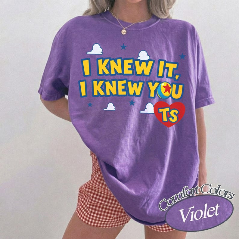 K&ouml;nnte beinhalten: Ein violettes Kurzarm-T-Shirt mit dem gelben Text I KNEW IT, I KNEW YOU TS, einem roten Herz, einem kleinen Ball mit rotem Stern und wei&szlig;en Wolkengrafiken. Das T-Shirt wird mit einer rot-wei&szlig; karierten Shorts kombiniert.