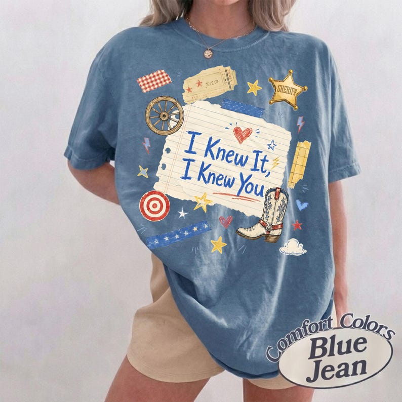 Puede incluir: Una camiseta azul con un estampado gr&aacute;fico de un trozo de papel rayado con el texto I Knew It, I Knew You. El dise&ntilde;o incluye una bota de vaquero, una estrella de sheriff, una rueda de carreta, una diana y varias estrellas y corazones.