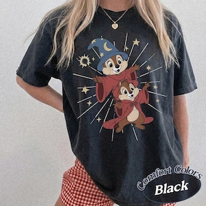 Op de afbeelding: Zwart Comfort Colors T-shirt met een cartoon illustratie van twee chipmunks in tovenaarskostuums, een met een blauwe hoed en toverstaf. Het ontwerp bevat sterren en de tekst "Comfort Colors Black".