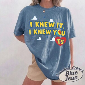 K&ouml;nnte beinhalten: Ein blaues T-Shirt in Jeansoptik mit dem gelben Text I KNEW IT, I KNEW YOU, einem roten Herz mit den Buchstaben TS, einer bunten Ballgrafik und wei&szlig;en Wolkenformen. Das T-Shirt hat einen Rundhalsausschnitt und kurze &Auml;rmel in lockerer Passform.
