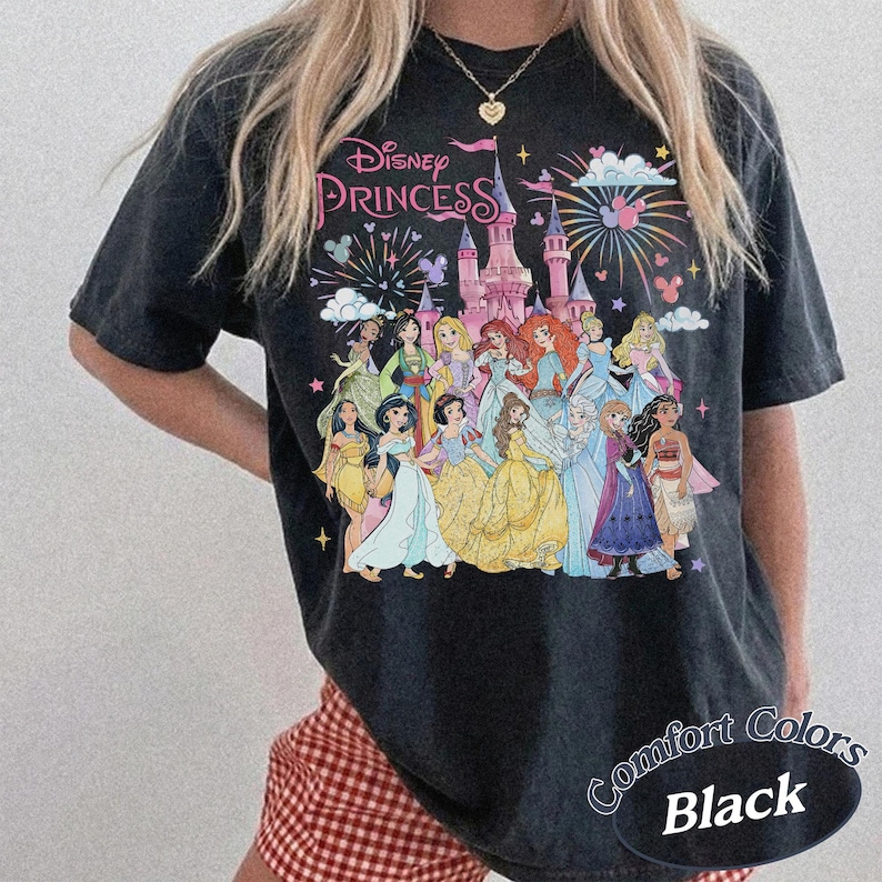 May include: Black t-shirt featuring a graphic of Disney Princesses in front of a castle with fireworks. The text "Disney Princess" is above the castle. The shirt has the text "Comfort Colors Black" on the bottom right.