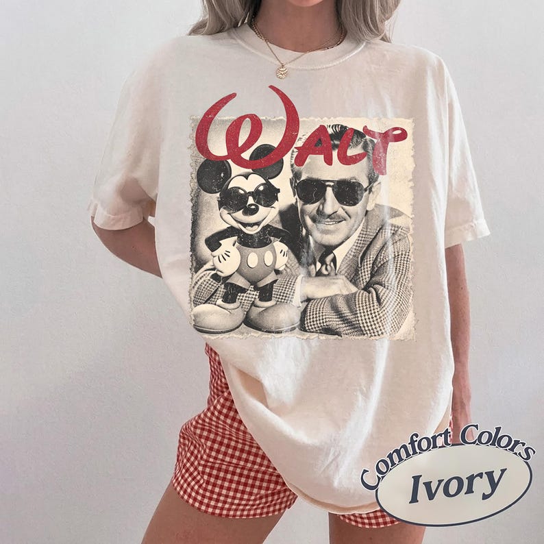 May include: Ivory-colored t-shirt featuring a vintage graphic of Mickey Mouse and Walt Disney. The graphic includes the word "Walt" in red script. The shirt is a Comfort Colors brand.