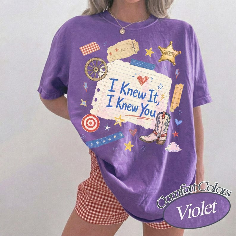 Puede incluir: Una camiseta morada de manga corta con un gr&aacute;fico central de papel de cuaderno rayado con el texto I Knew It, I Knew You. El dise&ntilde;o incluye una bota de vaquero, una estrella de sheriff, una rueda de carreta y varias estrellas y corazones.