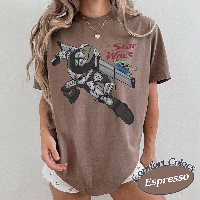 Pu&ograve; includere: T-shirt color espresso con grafica di un personaggio Mandaloriano con Grogu di Star Wars. Il design include il logo di Star Wars. La maglietta fa parte della collezione Comfort Colors.
