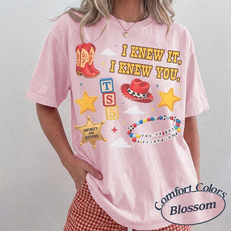 Pode incluir: Uma t-shirt rosa claro com o texto I KNEW IT, I KNEW YOU, juntamente com gr&aacute;ficos de botas de cowboy vermelhas, um chap&eacute;u de cowboy vermelho, blocos de letras T S 5, estrelas amarelas, uma estrela de xerife e uma pulseira de contas.