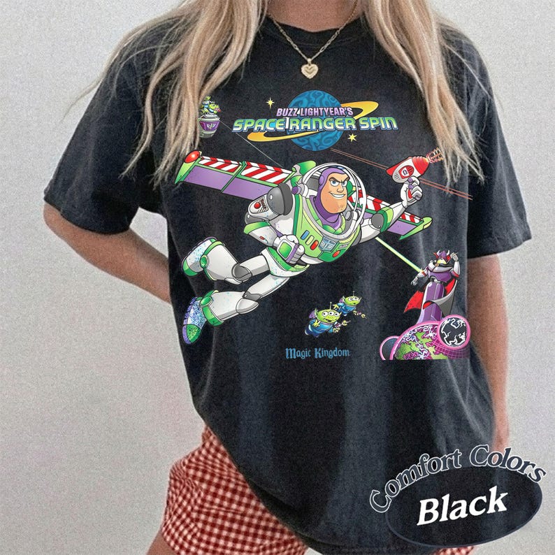 May include: Black t-shirt featuring a graphic of Buzz Lightyear from Toy Story in a Space Ranger design. The shirt includes the text "Buzz Lightyear's Space Ranger Spin" and "Magic Kingdom". The shirt is part of the Comfort Colors collection.