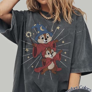 Op de afbeelding: Donkergrijs t-shirt met een cartoon illustratie van twee chipmunks verkleed als tovenaars, een met een toverstaf. De chipmunks dragen rode gewaden en blauwe tovenaars hoeden. De tekst "Comfort Colors Pepper" staat rechtsonder.