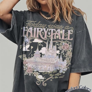 Może przedstawiać: Ciemnoszary t-shirt z nadrukiem przedstawiającym zamek, motyle i kwiaty. Napis głosi "Today was a FAIRY TALE" oraz "Can you feel this magic in the air?". W dolnym rogu znajduje się oznaczenie "Comfort Colors Pepper".