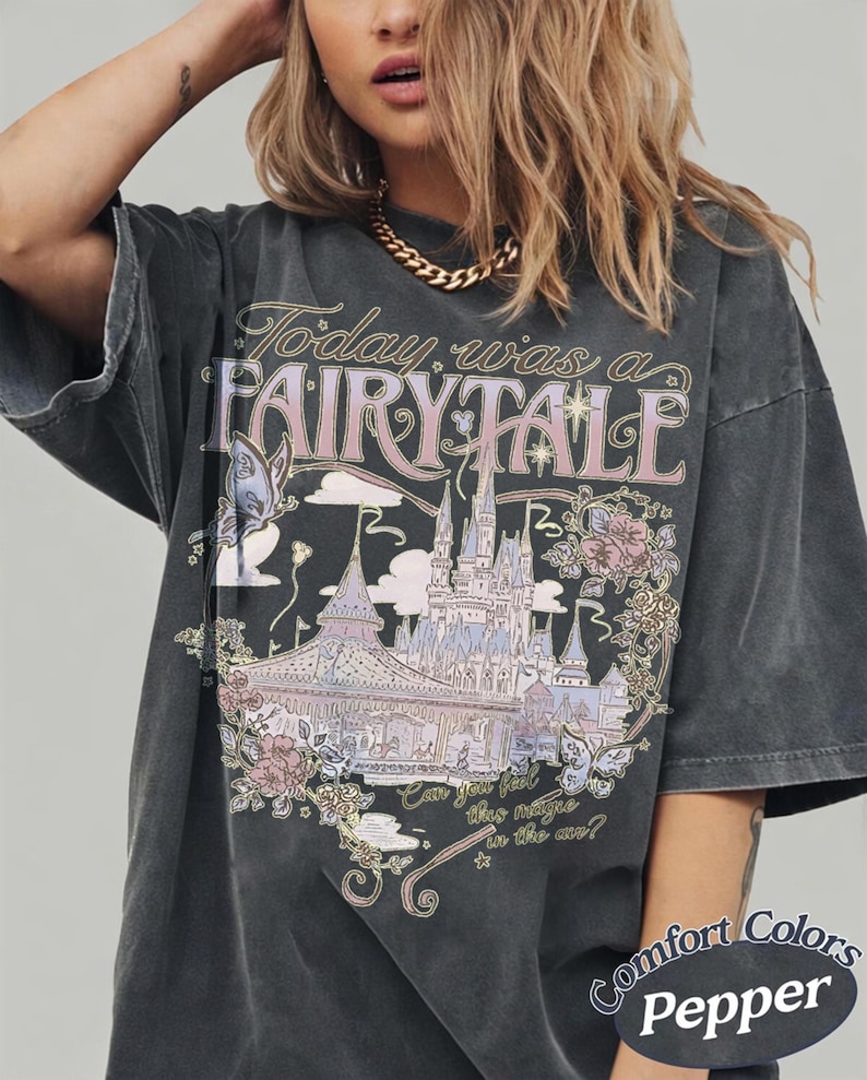 Może przedstawiać: Ciemnoszary t-shirt z nadrukiem przedstawiającym zamek, motyle i kwiaty. Napis głosi "Today was a FAIRY TALE" oraz "Can you feel this magic in the air?". W dolnym rogu znajduje się oznaczenie "Comfort Colors Pepper".