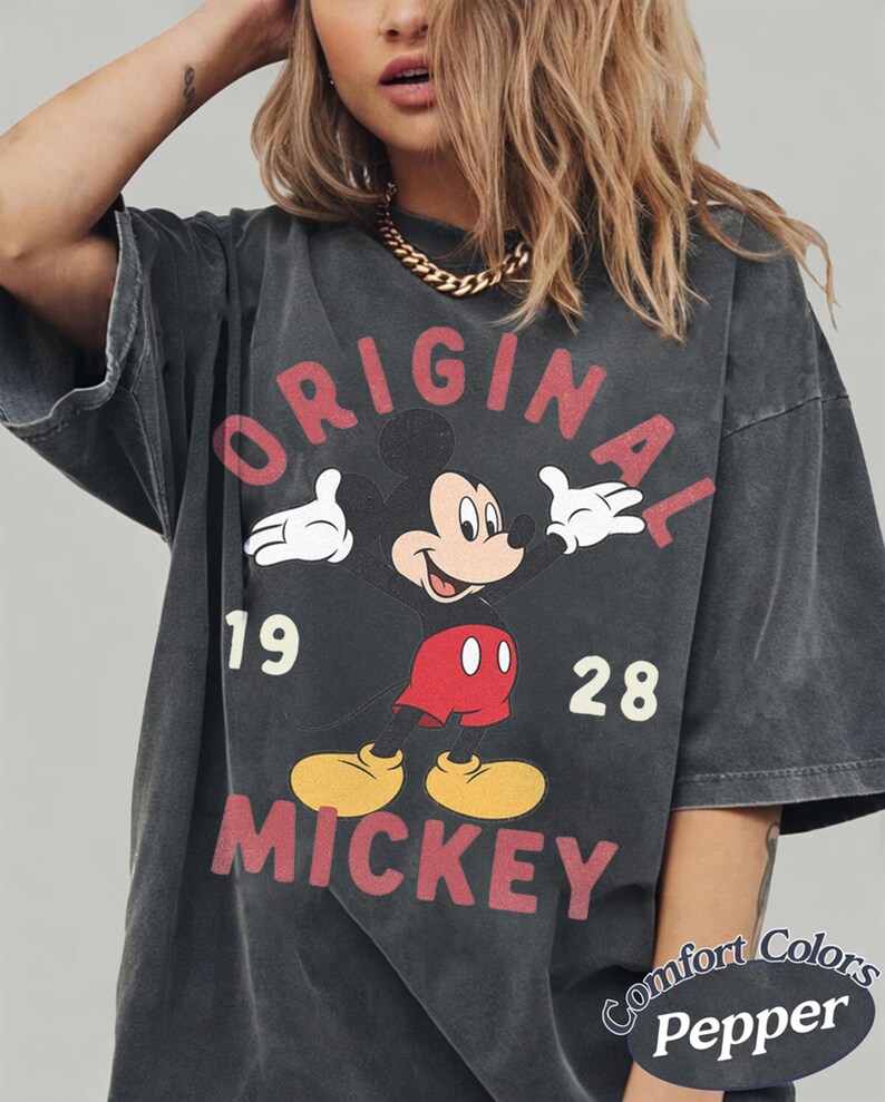 Op de afbeelding: Een antracietgrijs T-shirt met korte mouwen en een afbeelding van Mickey Mouse met de tekst ORIGINAL MICKEY 19 28. Het shirt heeft een vervaagde uitstraling en bevat een klein rond logo in de hoek met de tekst Comfort Colors Pepper.