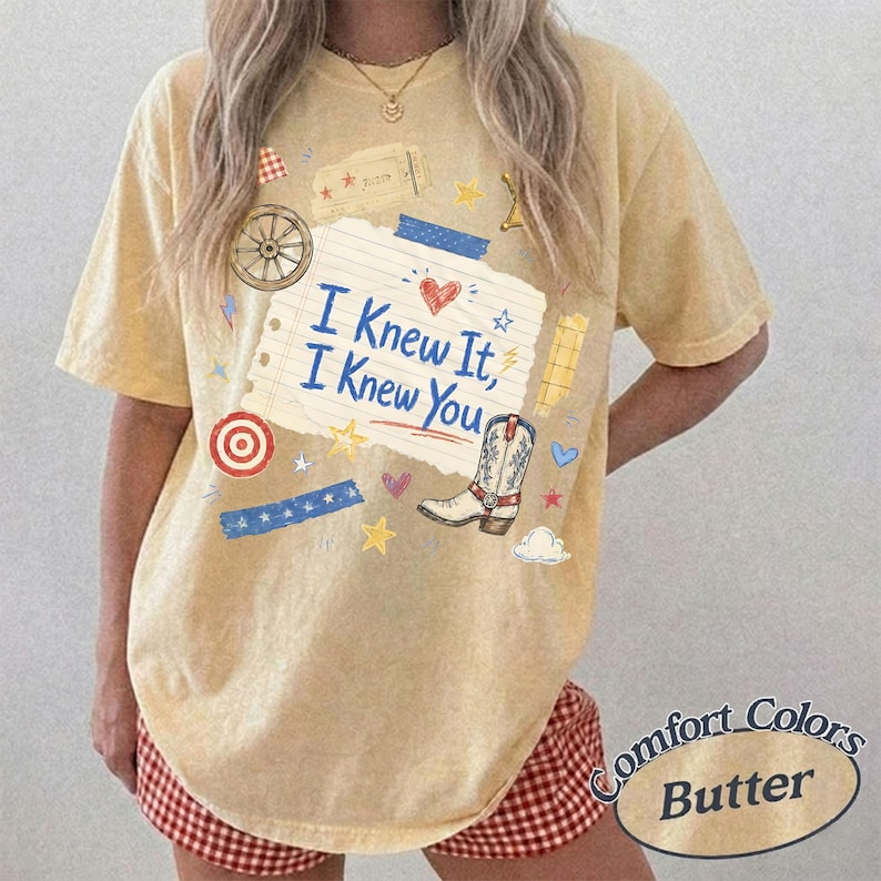 Puede incluir: Una camiseta de manga corta de color amarillo p&aacute;lido con un estampado gr&aacute;fico de una nota de papel rayado con el texto I Knew It, I Knew You, una bota vaquera, una rueda de carreta, una diana, estrellas, corazones y cintas azules.