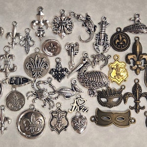 May include: A collection of silver-toned metal charms featuring various designs, including fleur-de-lis, crowns, pelicans, crabs, lobsters, and a Mardi Gras mask.