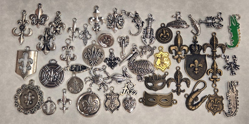 May include: A collection of silver-toned metal charms featuring various designs, including fleur-de-lis, crowns, pelicans, crabs, lobsters, and a Mardi Gras mask.