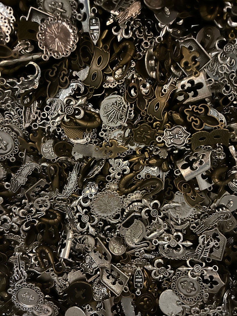May include: A large pile of silver and bronze metal charms, including fleur-de-lis, anchors, and other decorative designs.