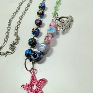 May include: A handmade necklace featuring a silver chain, colorful beads, and a pink wire star pendant. The necklace includes a charm with the text "I WANT TO BELIEVE". The beads are in various colors, including blue, pink, and green.