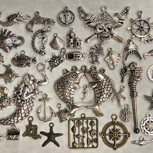 May include: A collection of silver-toned metal charms with nautical and sea life themes. The charms include a variety of shapes, such as anchors, fish, seashells, starfish, mermaids, and a pirate skull.
