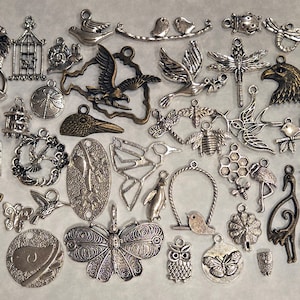 May include: A collection of silver-toned metal charms featuring various animal, nature, and abstract designs. The charms include birds, butterflies, owls, dragonflies, a birdcage, a flamingo, a bee, a honeycomb, and more.