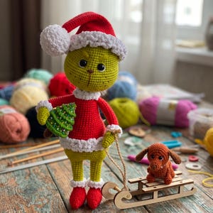 May include: A crocheted green character doll wearing a red Santa hat and suit with white trim, holding a small green Christmas tree. A small brown crocheted dog sits on a wooden sled attached to the doll by a string, all made of yarn.