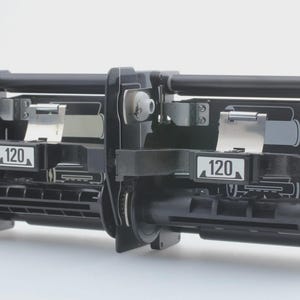 May include: A black mechanical device with the number "120" displayed on a white rectangle. The device has multiple parts, including rollers, levers, and a gear. The background is plain white.