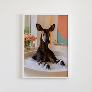 Puede incluir: Una lámina de arte mural enmarcada que muestra un okapi de pelaje marrón oscuro y patas con rayas blancas sentado en una bañera redonda blanca llena de espuma. El baño incluye un grifo dorado, flores rosas y un cuadro abstracto enmarcado.