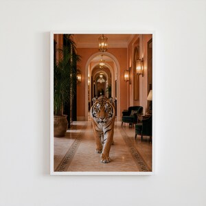 May include: A framed print of a tiger walking towards the viewer in a long hallway. The tiger has orange and black stripes. The hallway has a peach-colored wall, ornate lighting, and dark green chairs.