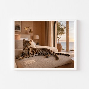 May include: A framed print showing a leopard relaxing on a beige sofa. The leopard's coat is patterned with spots. The room is bathed in sunlight, with a view of the sea. The decor has a neutral colour scheme.