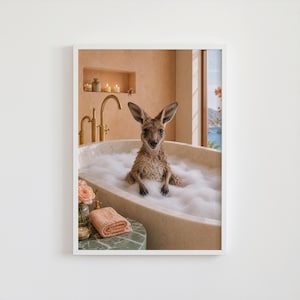 以下が含まれることがあります： 白い泡で満たされた大理石のバスタブに座るカンガルーを描いた額装アートプリント。バスルームは温かみのあるベージュの壁、ゴールドの蛇口、ピンクの花が入った小さな花瓶、折りたたまれたピーチ色のタオルが特徴です。